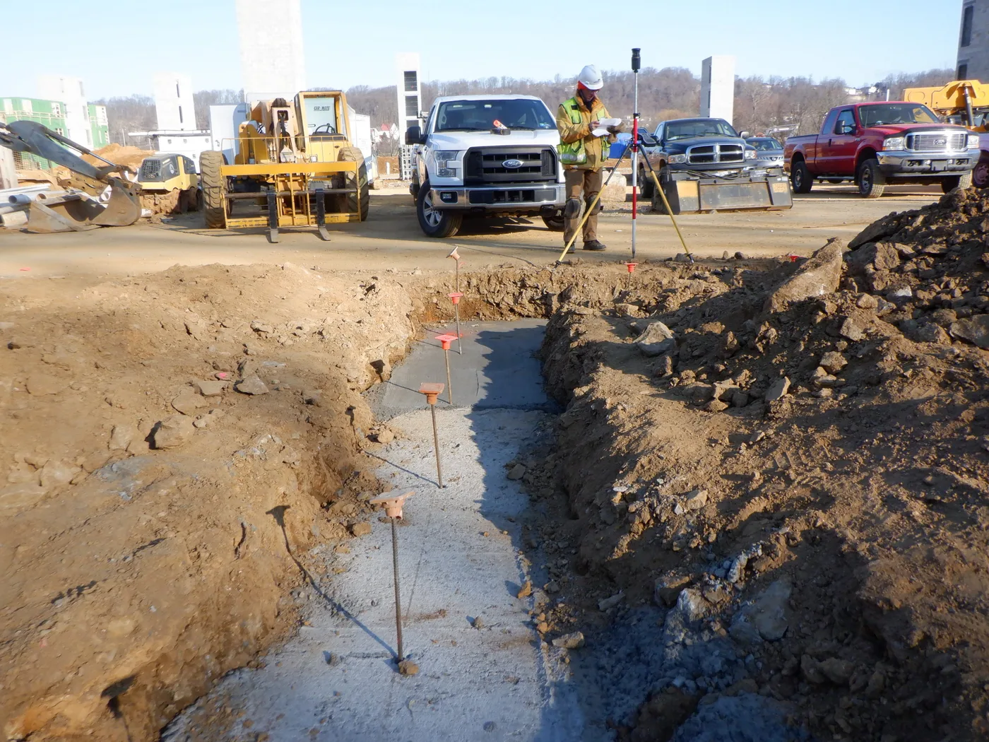 Crew working a house pad and footing excavation with trucks staged behind
